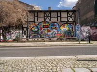 a wall with different colorful artwork on it in a city with buildings around and the street has a bike path going under it