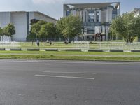 an open street in front of a building with a green grass field next to it