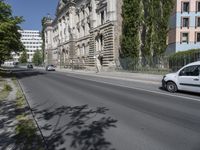 cars driving on the street next to a building with two stories and trees on each side