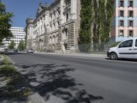 cars driving on the street next to a building with two stories and trees on each side