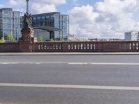 a statue on a stone railing near a road with buildings in the background with a street light next to it