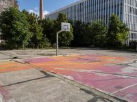 an abandoned basketball court with graffiti on it in a big building area with trees around