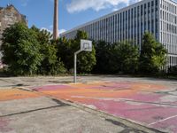 an abandoned basketball court with graffiti on it in a big building area with trees around