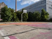 an abandoned basketball court with graffiti on it in a big building area with trees around