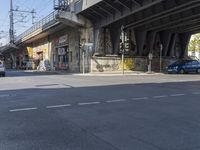 an empty street in front of an overpass with graffiti on it and cars driving down the street