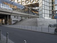 a man rides his bike down an empty street near a building with tall glass walls