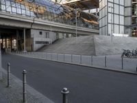 a man rides his bike down an empty street near a building with tall glass walls