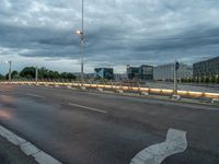 a road on an empty city street under a cloudy sky at dusk with traffic lights