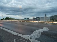 a road on an empty city street under a cloudy sky at dusk with traffic lights