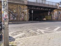 this is an intersection with a bike path underneath a bridge and graffiti on the side of the road