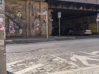 this is an intersection with a bike path underneath a bridge and graffiti on the side of the road