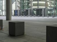 three gray concrete blocks standing in front of a tall glass building next to a sidewalk