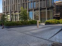 the side walk of a glass office building with concrete bricks and landscaping on each floor