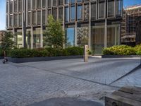 the side walk of a glass office building with concrete bricks and landscaping on each floor