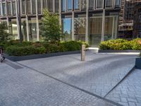 the side walk of a glass office building with concrete bricks and landscaping on each floor