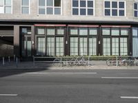 several bikes are parked in front of a tall building with many windows and shuttered glass