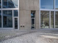 a grey brick sidewalk and some glass buildings and people standing outside of a building with people looking out the windows