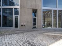 a grey brick sidewalk and some glass buildings and people standing outside of a building with people looking out the windows