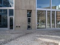 a grey brick sidewalk and some glass buildings and people standing outside of a building with people looking out the windows