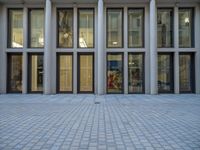 an empty brick courtyard area with two stone columns and two arched windows in the background