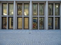 an empty brick courtyard area with two stone columns and two arched windows in the background