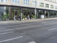 a group of people stand around near the sidewalk in front of a building with many windows