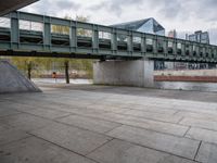 an image of city street under a green bridge in the day time with water and people walking around