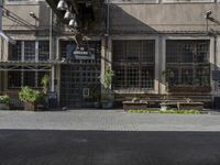 some old buildings and a street and bushes and a brick floored sidewalk outside of a restaurant