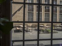 a window view of benches on a courtyard by a building, with leaves and greenery behind them