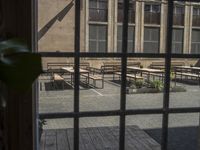 a window view of benches on a courtyard by a building, with leaves and greenery behind them