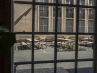 a window view of benches on a courtyard by a building, with leaves and greenery behind them