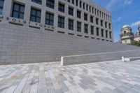 a woman sitting on a brick floor by a wall and building under a bright blue sky