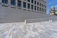 a woman sitting on a brick floor by a wall and building under a bright blue sky