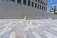 a woman sitting on a brick floor by a wall and building under a bright blue sky