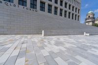 a woman sitting on a brick floor by a wall and building under a bright blue sky