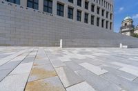 a woman sitting on a brick floor by a wall and building under a bright blue sky