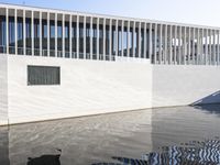 a person walking down a sidewalk in front of a building with windows over the water