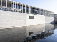 a person walking down a sidewalk in front of a building with windows over the water