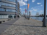 an image of a brick walkway on the side of the water near a tall building