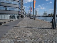 an image of a brick walkway on the side of the water near a tall building