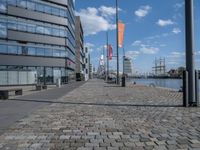 an image of a brick walkway on the side of the water near a tall building