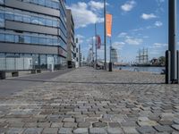 an image of a brick walkway on the side of the water near a tall building