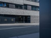 the exterior of a gray building with glass windows on the side walk with black and white logo in front