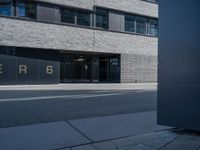 the exterior of a gray building with glass windows on the side walk with black and white logo in front