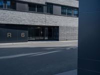 the exterior of a gray building with glass windows on the side walk with black and white logo in front