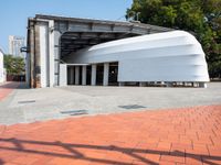 a white building with a roof in the middle of a sidewalk and a tree next to it