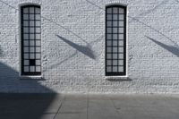 two windows on the white brick wall of an empty building in the shadows of another window