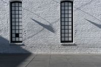 two windows on the white brick wall of an empty building in the shadows of another window