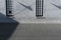 two windows on the white brick wall of an empty building in the shadows of another window