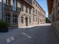 a view of a bricked side walk in an industrial building, with windows on two sides of the walkway